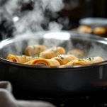 Involtini di pollo che cuociono coperti in padella.