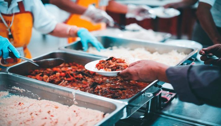 persona che riceve un piatto di cibo in mensa