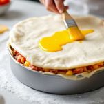 Farcitura livellata e coperta con disco di pasta, spennellata con tuorlo