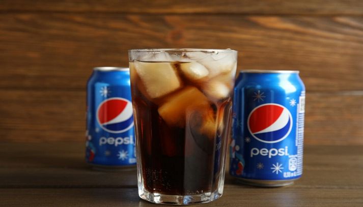 Bicchiere di Pepsi con ghiaccio e lattine sullo sfondo