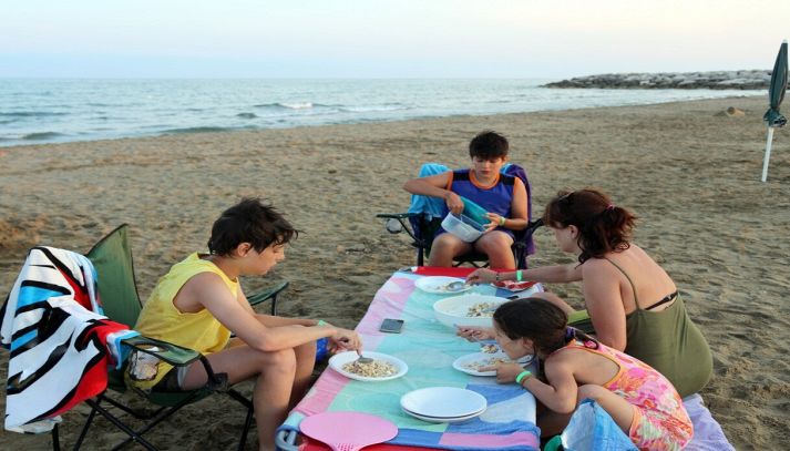 Famiglia mangia sulla spiaggia al tramonto