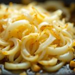 Cipolla tritata che cuoce in padella con olio mentre una pentola scalda il brodo vegetale