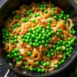 Piselli verdi versati in padella con cipolla rosolata mentre vengono mescolati con condimenti