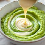 Crema di piselli in pentola mentre viene aggiunta la panna e mescolata sul fuoco