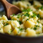 Patate schiacciate e prezzemolo tritato su tagliere.