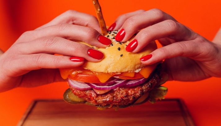 Donna con smalto rosso mangia un succulent hamburger