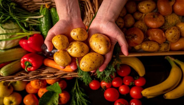 Mani con patate e ortaggi e frutta sullo sfondo