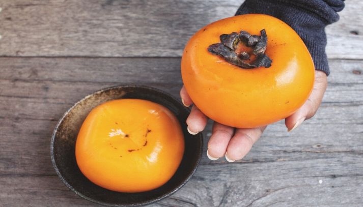 Mano stringe un gustoso cachi, mentre un secondo frutto è nella ciotola