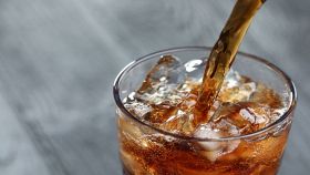 Versare la Coca Cola in un bicchiere di vetro con ghiaccio