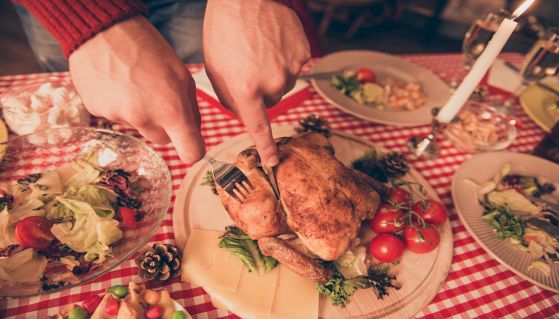 Uomo taglia il pollo sulla tavola natalizia