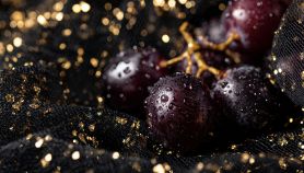 Uva scura con gocce d'acqua scintillanti poggiate su un ricco velluto nero
