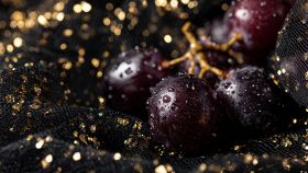 Uva scura con gocce d'acqua scintillanti poggiate su un ricco velluto nero