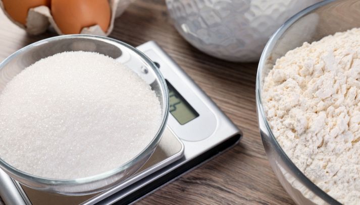 Ciotole con zucchero e farina su bilancia digitale da cucina con display; pesatura precisa degli ingredienti.