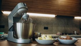 Impastatrice compatta con frusta e ciotola inox su piano cucina, ingredienti pronti per l’impasto.