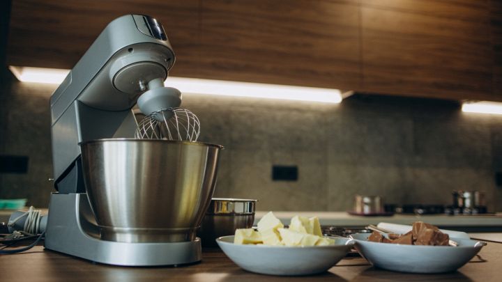 Impastatrice compatta con frusta e ciotola inox su piano cucina, ingredienti pronti per l’impasto.