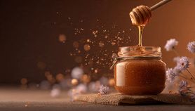 Miele che gocciola da un mestolo di legno in un barattolo