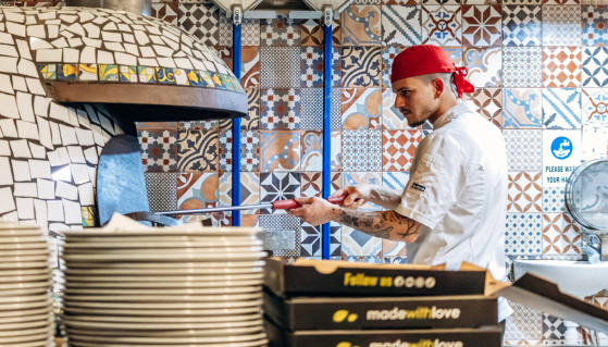 Forno e banco di una pizzeria con cartello cercasi pizzaiolo, tema carenza di personale e formazione nel settore