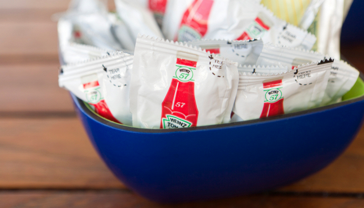 Bustine monodose di ketchup e maionese su un tavolo da ristorante, simbolo degli imballaggi usa e getta destinati a essere eliminati