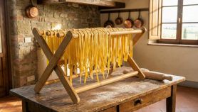 Stendipasta pieghevole in legno di bambù colmo di tagliatelle fresche, posizionato su un tavolo antico in una cucina rustica con mattarello e farina.