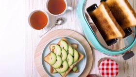 Tostapane moderno in acciaio inox con due fette di pane tostato fumanti e dorate, accompagnato da burro e marmellata su un tavolo da cucina.