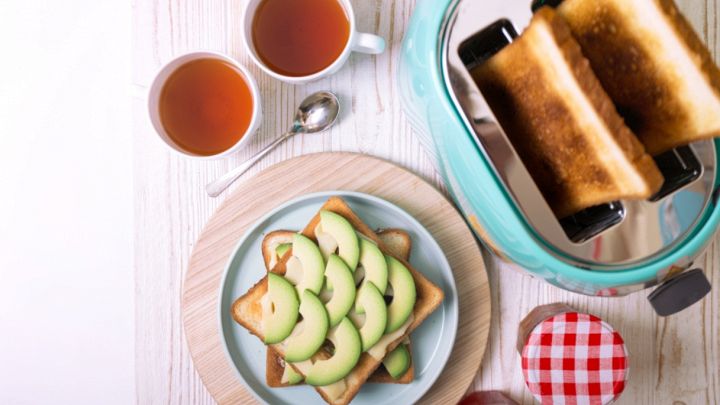 Tostapane moderno in acciaio inox con due fette di pane tostato fumanti e dorate, accompagnato da burro e marmellata su un tavolo da cucina.