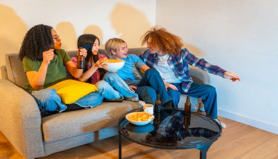 Amici guardano la tv sul divano, mangiando e bevendo in allegria
