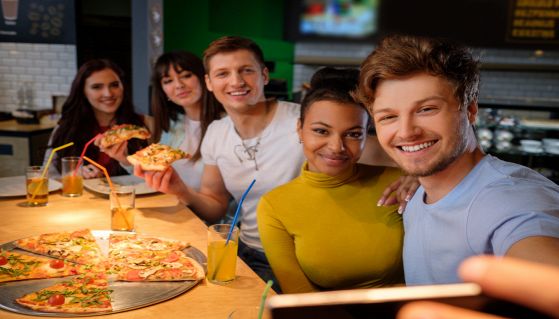 Amici si fanno un selfie mentre mangiano la pizza e guardano la tv