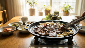 Primo piano di una griglia coreana da tavolo, in un'ambientazione domestica, illuminata da luce naturale calda e serena.