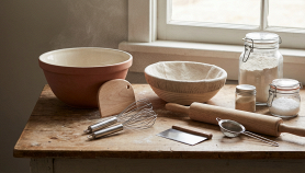 Primo piano di utensili da cucina essenziali per preparare impasti per pane, pizza e dolci con luce naturale e colori caldi.