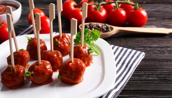 Piatto di polpette al sugo su un tavolo con spezie e pomodori freschi