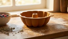 Stampo in silicone per dolci a forma di ciambella color terracotta, posato su un tavolo di legno infarinato accanto a una ciotola di frutti di bosco.