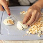 Donna taglia le uova sode a dadini su un tagliere