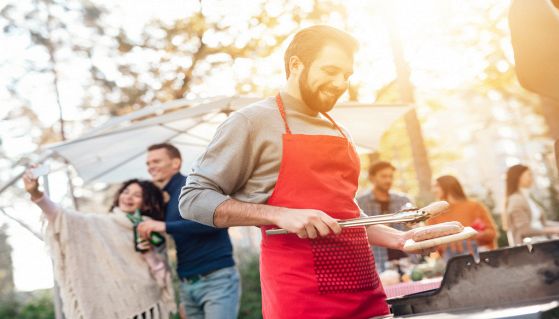Un uomo sta cucinando salsicce alla griglia a una festa di amici