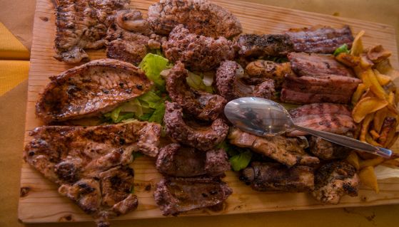 Vari tipi di carne cotti alla griglia con patate su tagliere di legno