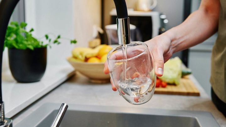 Una donna versa acqua potabile del rubinetto in un bicchiere