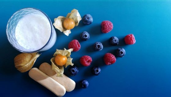 Frutti di bosco e un bicchiere di kefir su un ripiano azzurro
