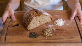 Pezzo di pane senza glutine su tagliere in legno con cereali e semi