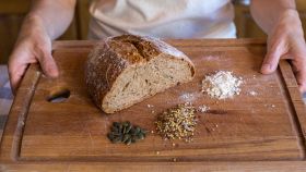 Pezzo di pane senza glutine su tagliere in legno con cereali e semi