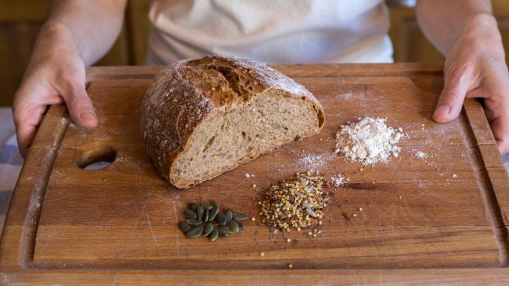 Pezzo di pane senza glutine su tagliere in legno con cereali e semi