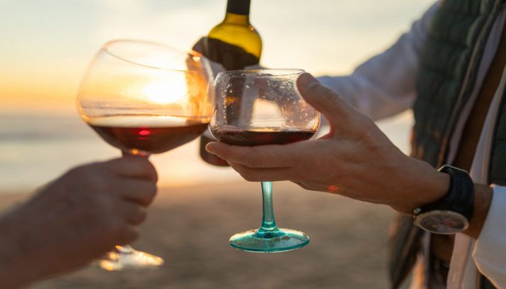 Persone brindano con calici di vino rosso al tramonto