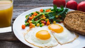 Un piatto di uova al tegamino, verdure lesse e pane abbrustolito con spremuta per colazione
