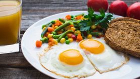Un piatto di uova al tegamino, verdure lesse e pane abbrustolito con spremuta per colazione