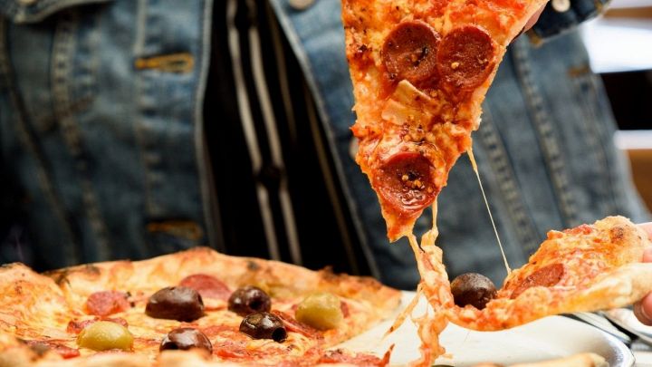 Un trancio tagliato da una pizza tonda con salame piccante e pronto da mangiare