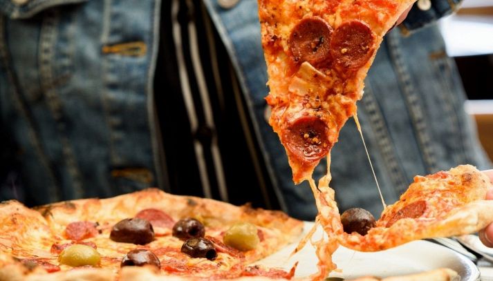 Un trancio tagliato da una pizza tonda con salame piccante e pronto da mangiare