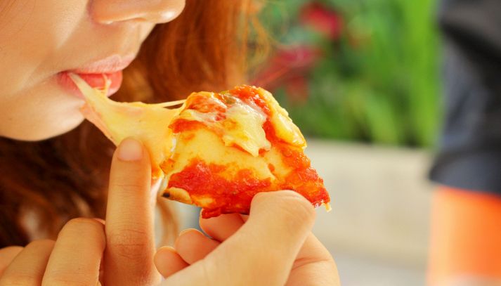 Ragazza mangia una gustosa e filante pizza margherita