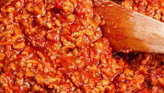 Macinato di carne al sugo per il ragù alla bolognese con cucchiaio di legno