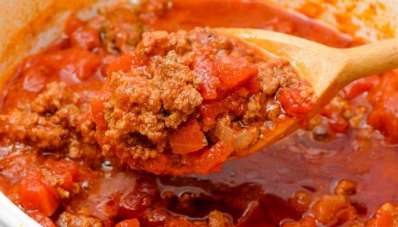 Cucchiaio immerso in un sugo pronto di ragù alla bolognese