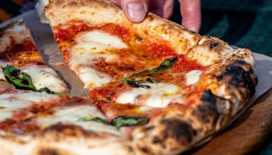 Una mano afferra un triangolo di una pizza margherita napoletana