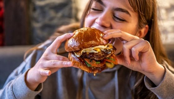 Una ragazza mangia un'hamburger doppio con pomodoro, insalata e cheddar