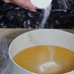 Una donna versa lo zucchero in un pentolino in cui c'è succo d'arancia